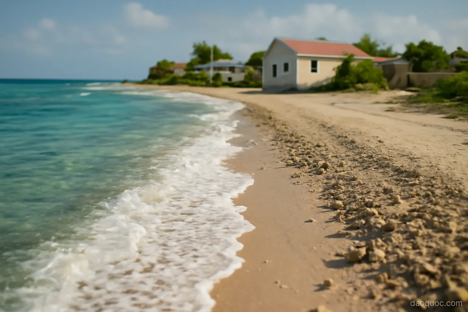 a low coral atoll with waves washing over a narrow strip of land near houses