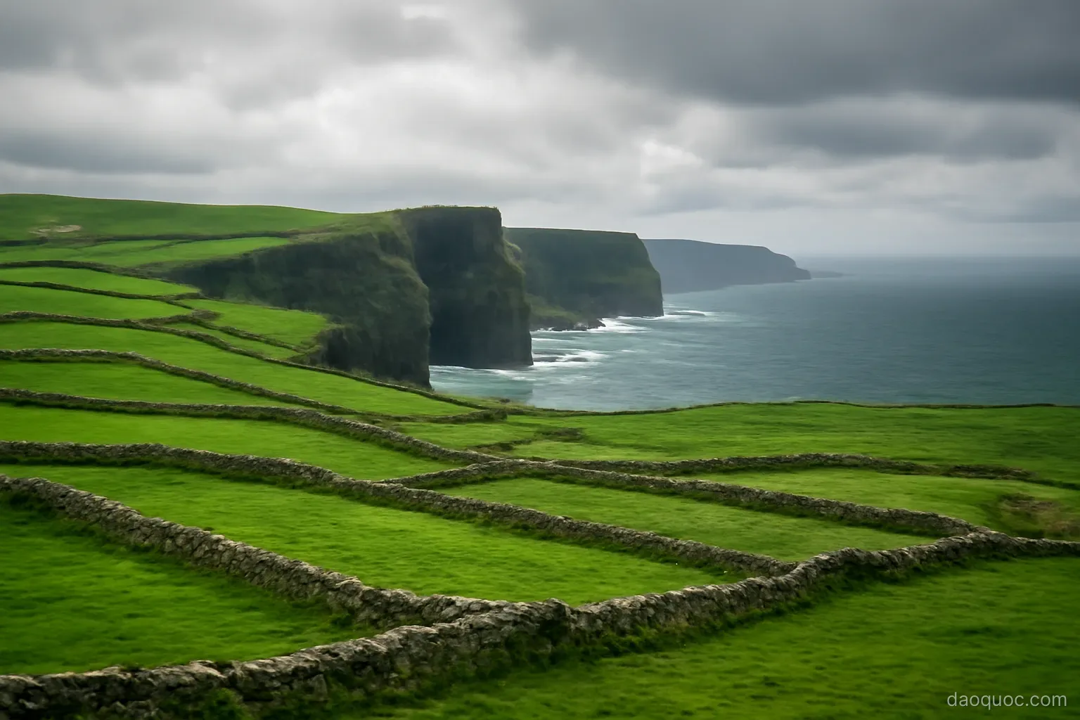 green rolling hills with stone walls meeting dramatic sea cliffs under grey clouds